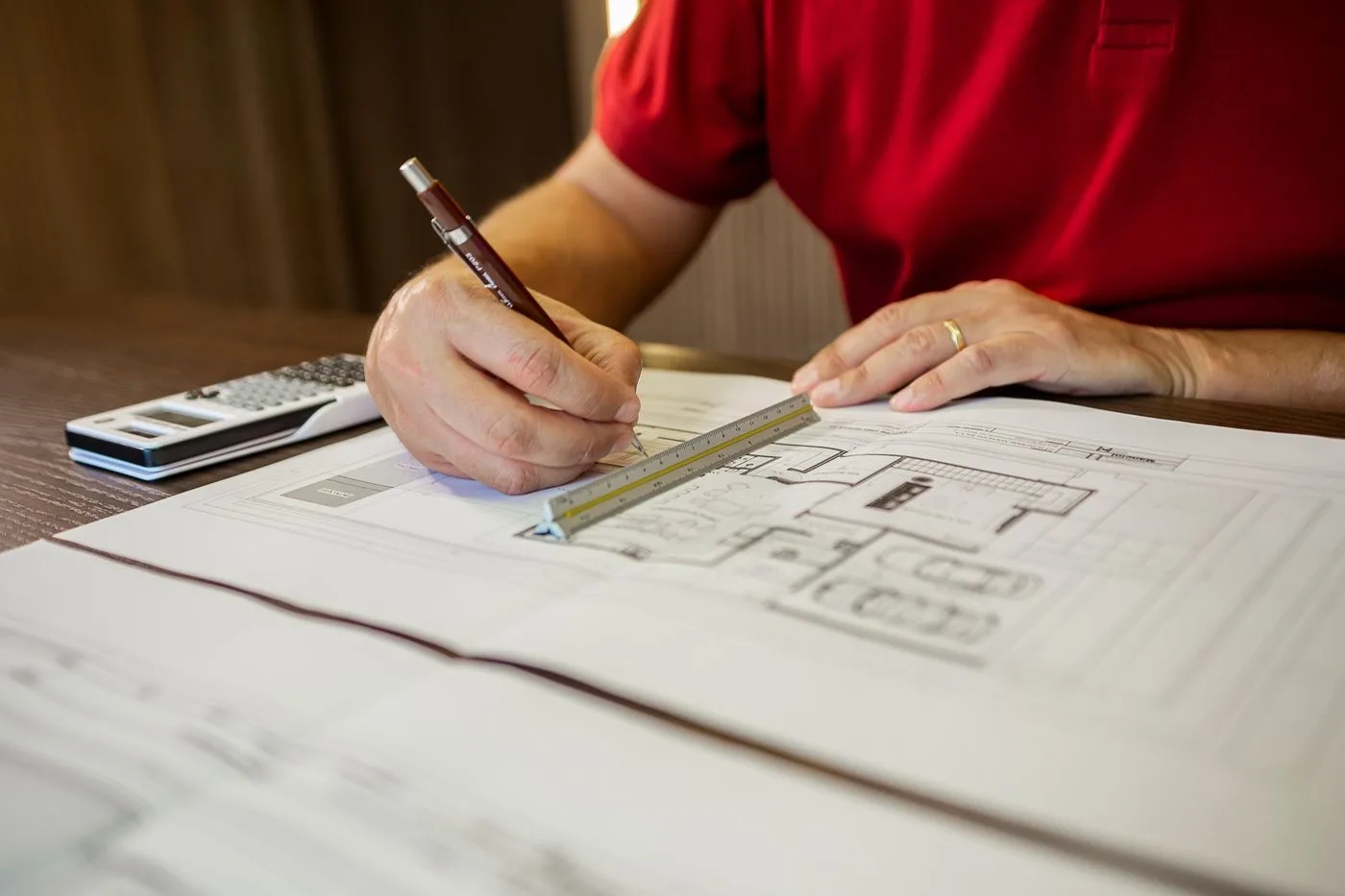 Main d'un professionnel traçant un plan de maison au crayon près d'une calculatrice, pour chiffrer un budget travaux